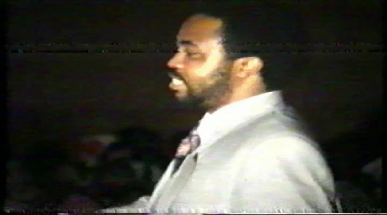 Reverend Adamson Aromaegbe preaching into a microphone in archival church footage.