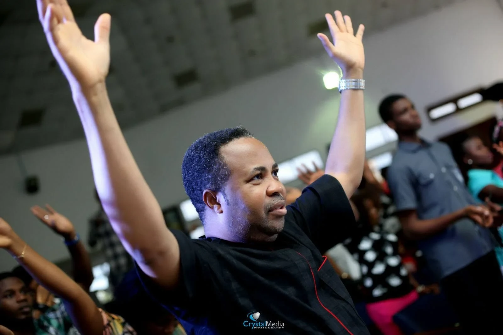 Reverend Aromaegbe with both arms raised during worship, with other worshippers behind him.